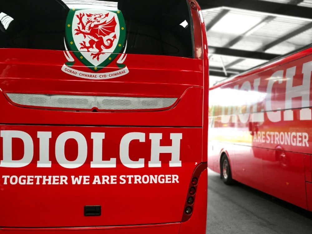 Close up of red vehicle wrap and white letter graphics on fleet of Welsh national football team coaches.