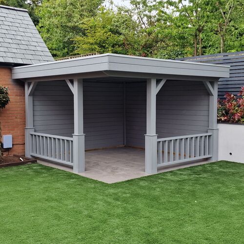 A bespoke garden gazebo supplied by Lugarde and designed and installed by Forevertimber. This elegant structure features a flat roof and a sleek grey-painted finish, blending seamlessly into modern garden designs. The gazebo is open-sided with decorative railing and sturdy wooden posts, while the back and side walls provide privacy and shelter. It is built on a neatly paved base, offering a durable and clean space for outdoor seating or entertaining. Positioned on a lush artificial grass lawn, the gazebo creates a stylish and functional addition to any garden.