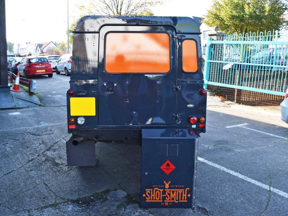 Rear end of company Land Rover Defender with blue wrap and orange branded vinyl graphics.