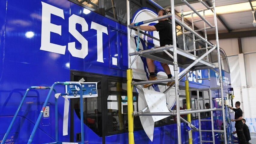 Vehicle wrap technicians installing Cardiff City livery and graphics on blue Alexander Dennis Enviro 400 double decker bus at Popin.