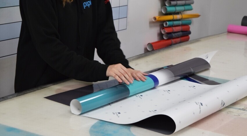 Vehicle wrap technician at Popin rolling out a printed livery.