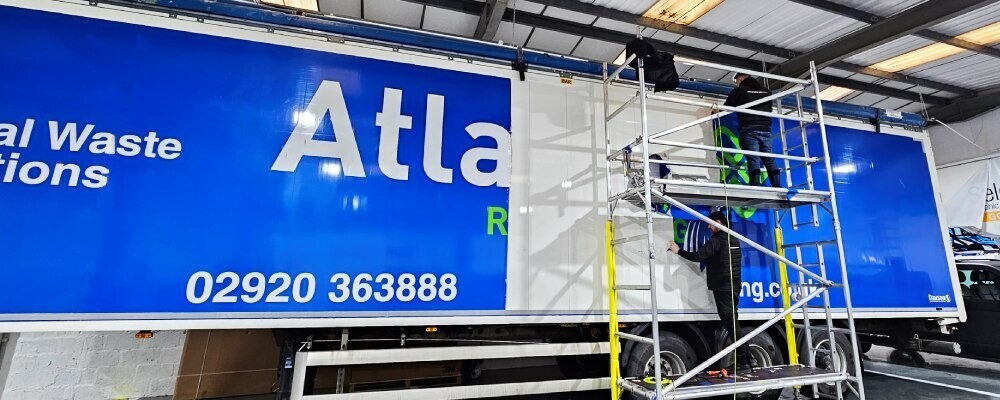 Installers at Popin in Cardiff applying a branded vinyl graphic to a large truck side panel.