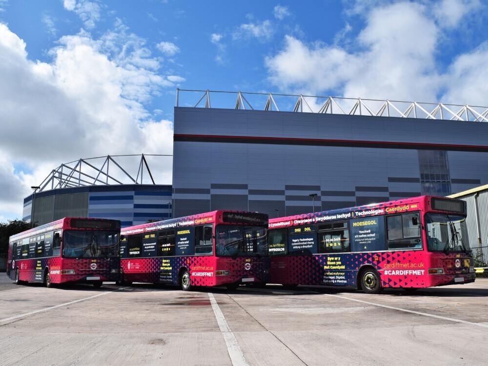 Fleet of three Dennis Dart Cardiff Bus vehicles with matching wraps outside football stadium.
