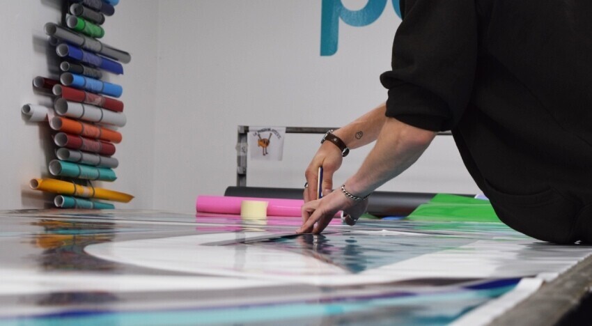 Vehicle graphics technician cutting vinyl material before installation on a Scania lorry.