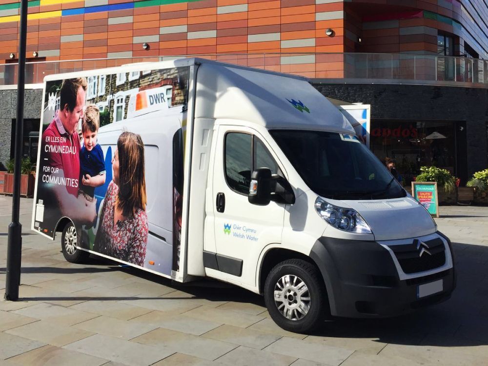 Large marketing campaign vinyl graphic on the side of a white Citroen Relay exhibition van in the city.