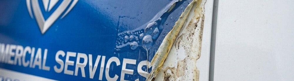 Close-up of a damaged blue and silver commercial vinyl vehicle wrap peeling and bubbling on a white van door panel.
