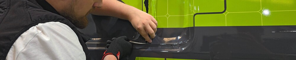 Vehicle wrap technician applying eco-friendly vinyl film to van panel.