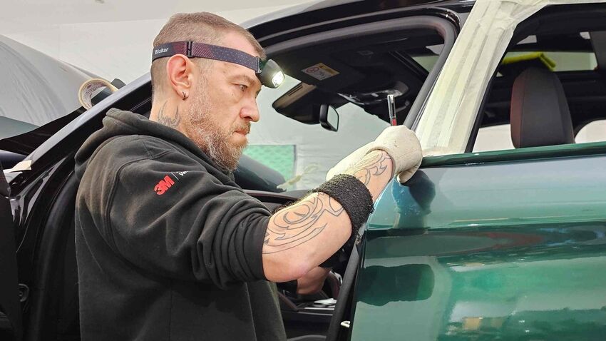 A vehicle wrap installer cutting vinyl material during installation on a car.