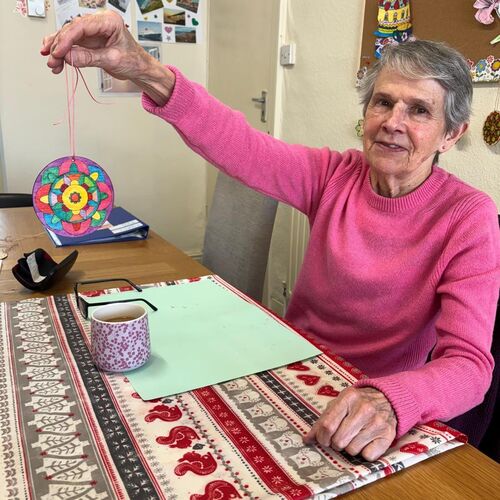 Elderly lady sat smiling, holding her artwork up at Your Care's Dementia Day Club in Hanham, Bristol