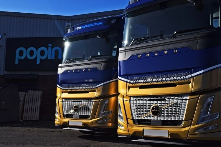 Matching blue and gold vehicle wraps on Volvo lorries outside Popin in Cardiff.