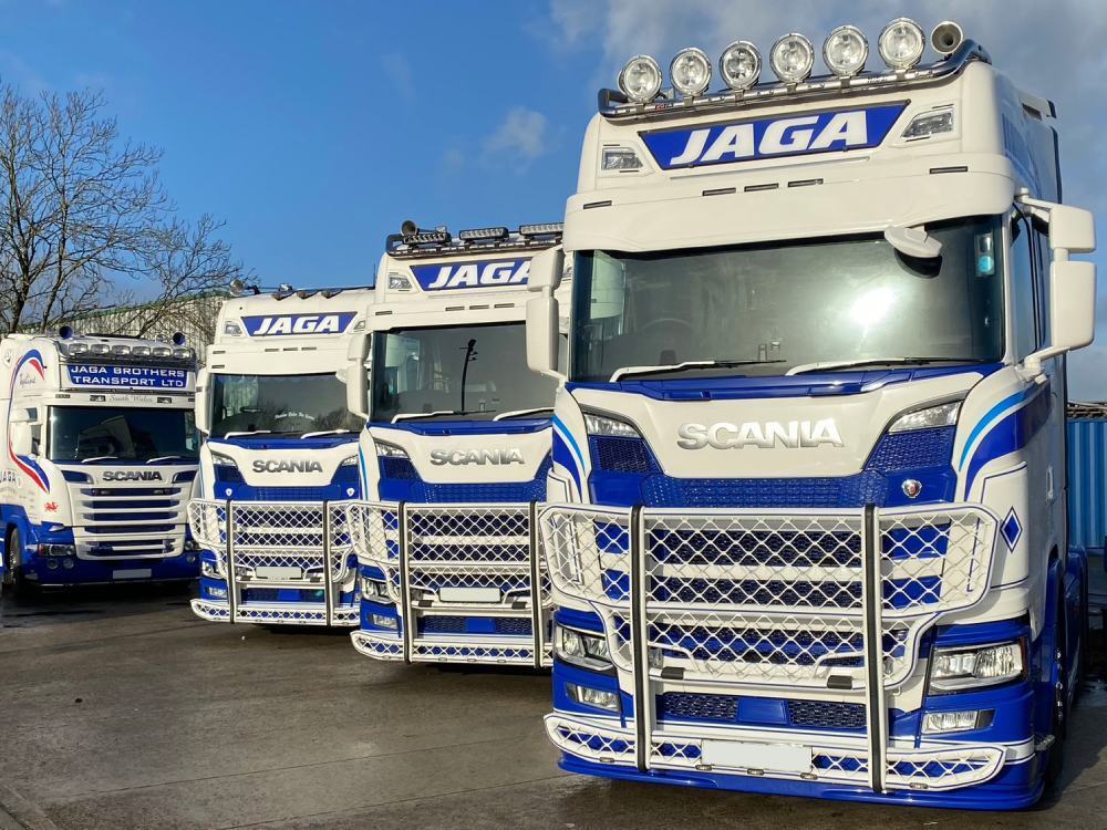 Fleet of Scania haulage trucks with matching vehicle wraps and graphics parked in a depot.