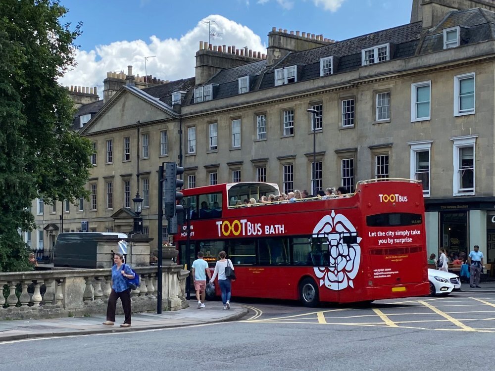 Red tour bus from a large fleet with new vehicle wrap and graphics driving through the town of Bath.