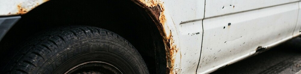 A close-up photograph showing realistic rust corrosion and bubbling paint around the wheel arch panel of a white commercial van.