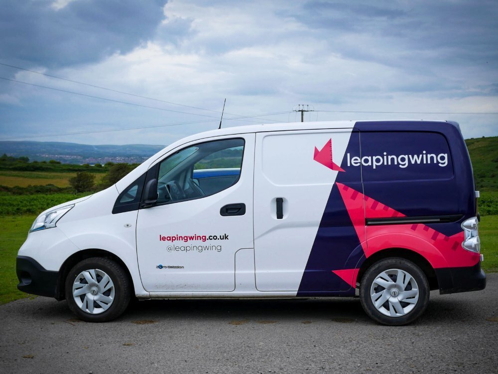 Nissan e-NV200 electric company van with Leaping Wing branded partial vehicle wrap.
