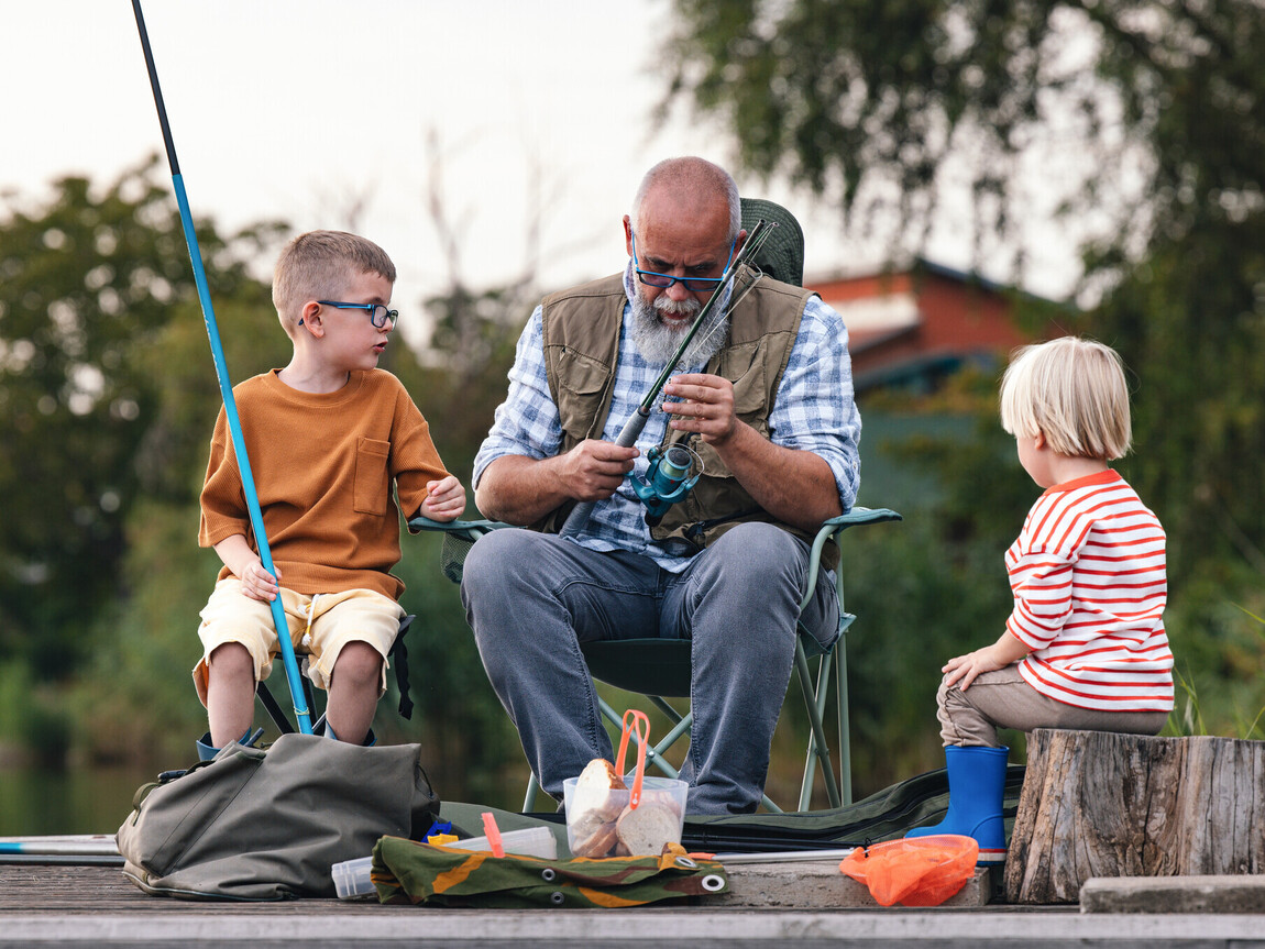 Grandfather Teaching Grandchildren How to Fish at Quiet Lake stock photo