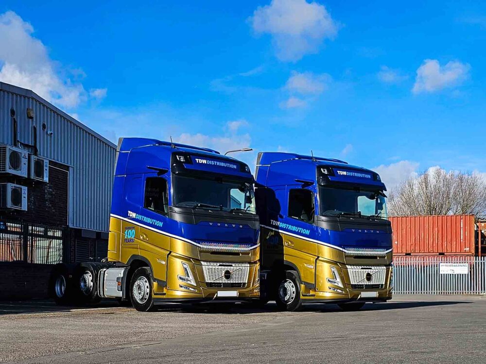 Company fleet of Volvo FH5 trucks with blue and gold wraps and branded vehicle graphics for TDW Distribution.