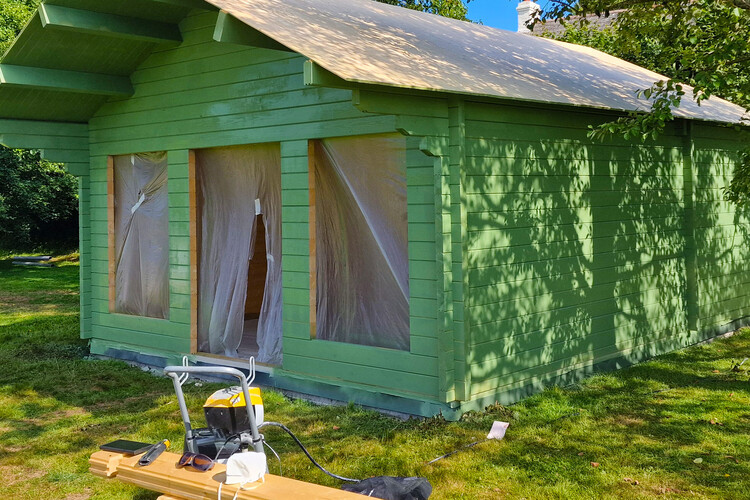 Partially constructed timber garden building painted in a vibrant green color, featuring large front windows and a central doorway, with protective coverings in place during the building process. The roof framework is visible, awaiting final installation, while the surrounding grassy area provides a natural setting. Tools and materials on-site indicate active progress on the project. This garden structure showcases durable craftsmanship and an attractive finish, making it ideal for use as a summerhouse, studio, or recreational space