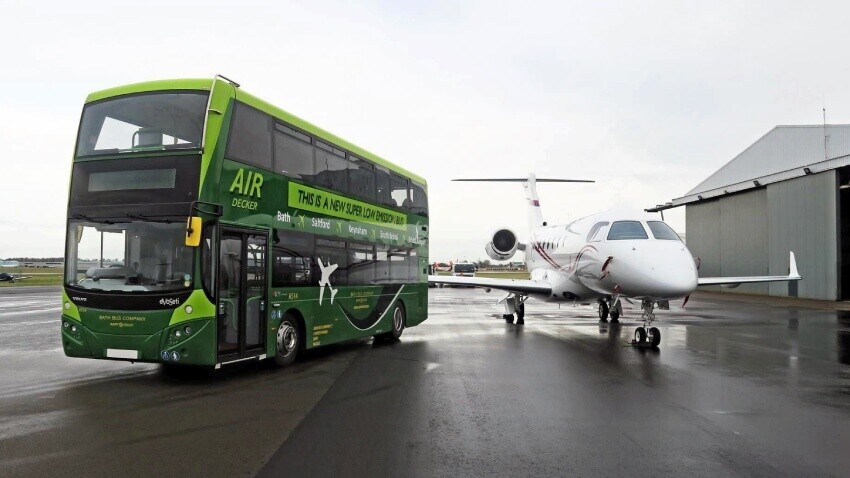 Volvo EvoSeti Air Decker with green Bath Bus Company vehicle wrap and graphics next to a plane.