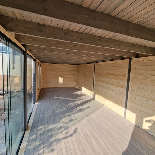 The interior of a bespoke timber garden building designed by Lugarde and crafted by Forevertimber. The space features a modern, open-plan layout with natural wooden paneling on the walls and ceiling, complemented by a matching wooden floor. Large sliding glass panels along one side flood the room with natural light, creating a bright and airy atmosphere. The exposed beams on the ceiling add a rustic yet contemporary charm, making it a versatile space suitable for a studio, office, or relaxation area.