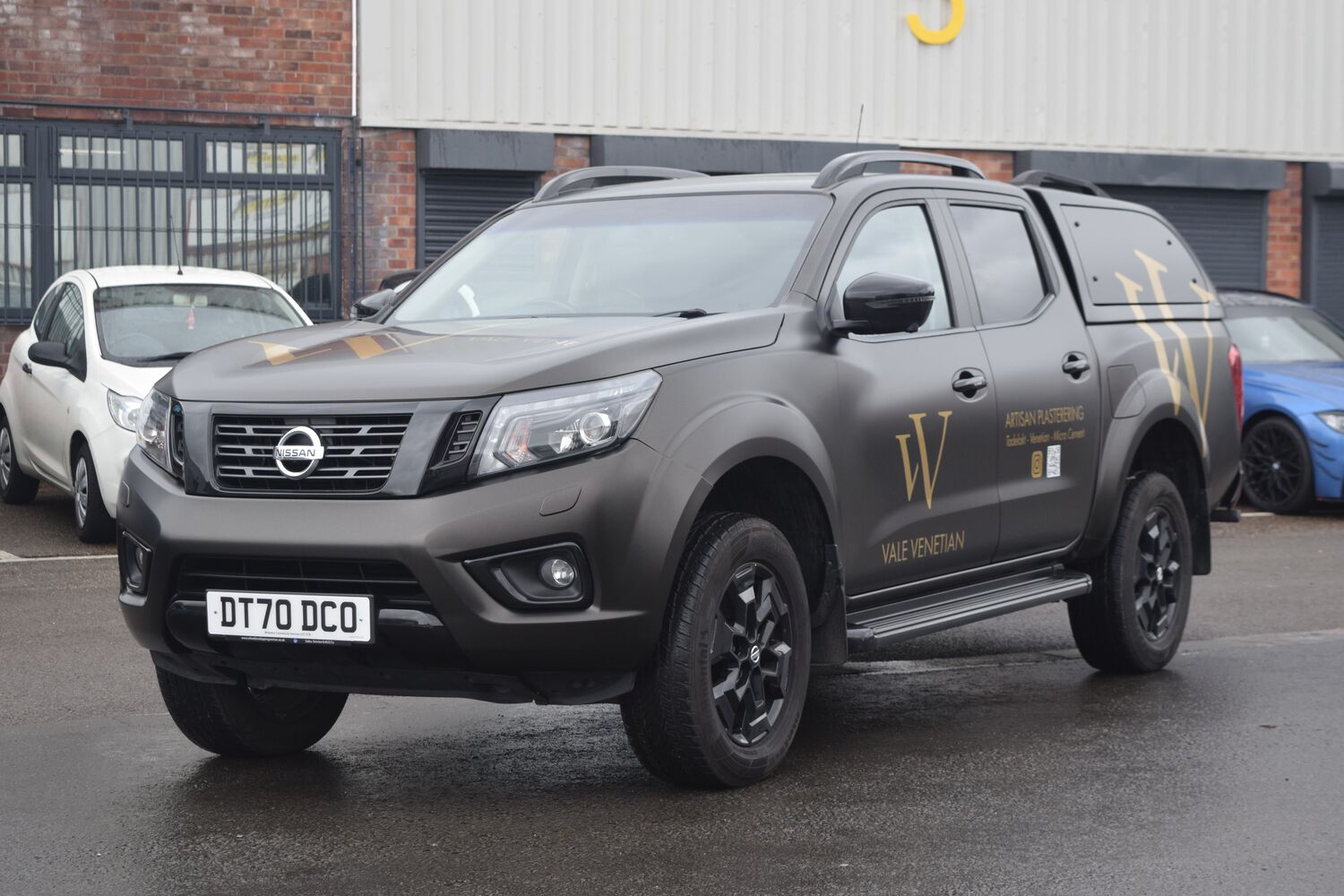 A Nissan Navara 4-door pickup truck with matte black vehicle wrap and Vale Venetian company branded gold vinyl graphics.