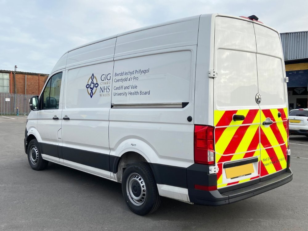 White Volkswagen Crafter with NHS vinyl graphics and rear chevron markings.