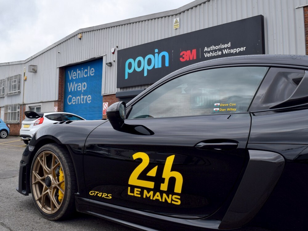 Front end of Porsche GT4 RS with black motorsport wrap and yellow race car graphics