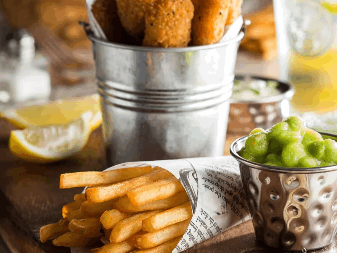 A photo of a meal on a table with chips wrapped in grease proof paper
