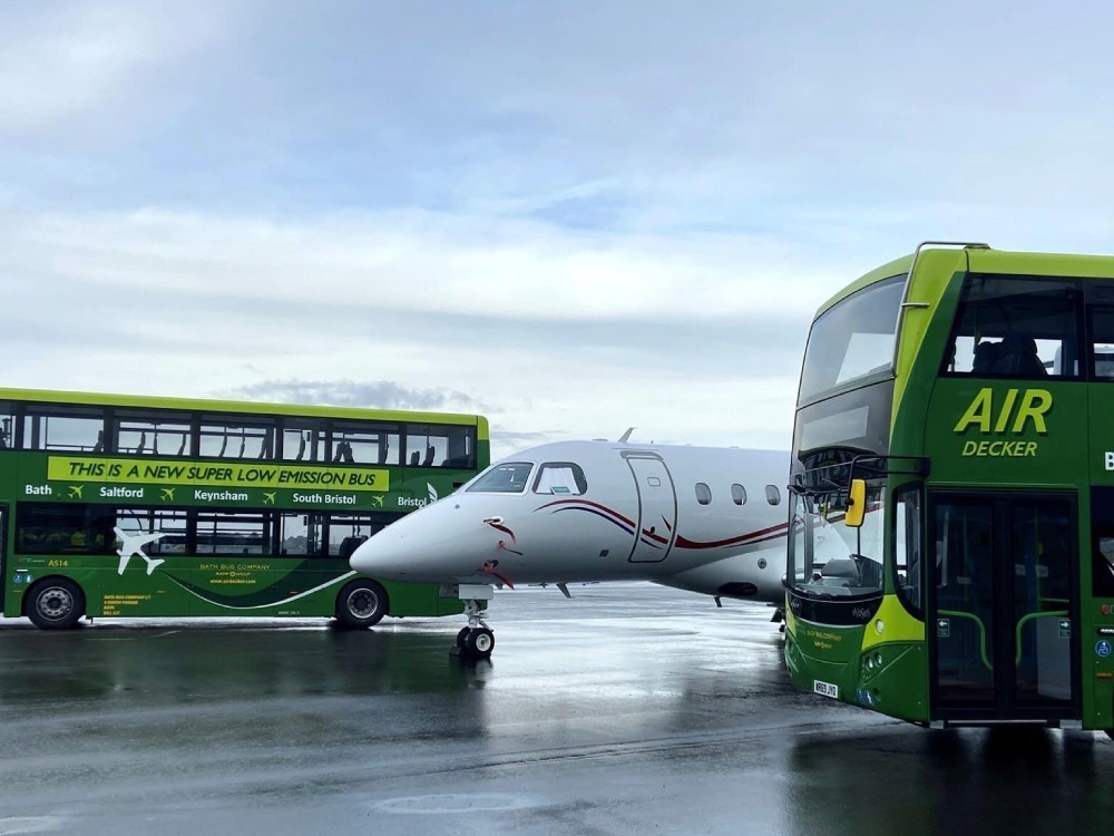 Green branded vehicle wraps on Bath Bus Company fleet parked on runway at airport.