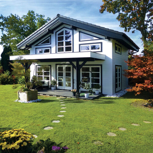 Modern two-story timber house with a sleek black and white design, featuring a pitched roof and large geometric windows that provide ample natural light. The front includes a spacious covered patio with black timber beams, creating a comfortable outdoor living space. A stepping-stone pathway leads to the house, surrounded by a lush, well-maintained lawn and colorful landscaping, including vibrant autumn foliage and decorative planters. Supplied by Bertsch Holzbau and expertly designed and installed by Forever Timber, this house combines contemporary architectural style with high-quality craftsmanship and natural beauty.