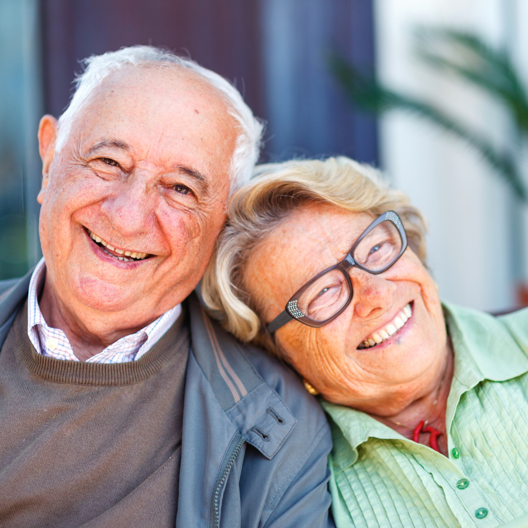 Smiling elderly couple sitting closely together at home in Bristol, showing comfort, companionship and wellbeing in later life