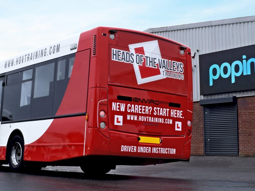 Company branded vinyl graphics on rear end of red and white driver training Alexander Dennis Enviro 300 bus outside Popin in Cardiff.