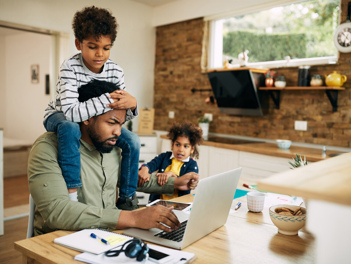 dad on his laptop trying to work with two small children climbing on him