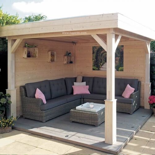 Elegant timber garden seating area supplied by Lugarde and designed and installed by ForeverTimber. This open-sided wooden structure features a cozy corner seating arrangement with a weather-resistant rattan sofa adorned with soft cushions in muted tones. The flat roof and sturdy posts offer a blend of modern design and practicality, providing shade and shelter for outdoor relaxation. Set on a durable wooden deck, this garden building is ideal for creating a tranquil retreat in any outdoor space.