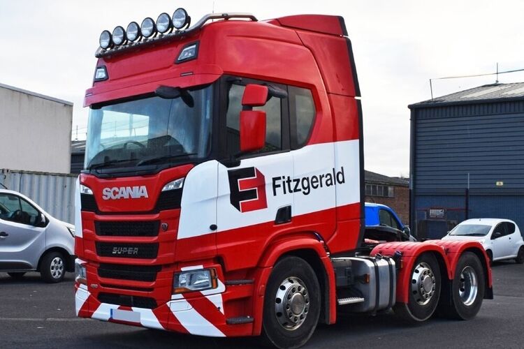 Red and white vehicle livery with company branded graphics on a Scania lorry cab.
