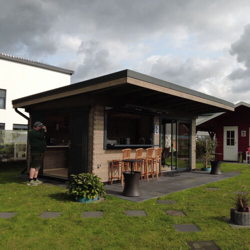 Modern timber outdoor pavilion with a sleek flat roof and open-concept design, featuring a stylish bar area with high wooden stools. The structure includes a blend of natural wood and glass elements, providing a seamless indoor-outdoor experience. Sliding glass doors and louvered panels enhance functionality and aesthetics, allowing for both privacy and ventilation. Set on a dark stone patio and surrounded by a well-maintained lawn with stepping stones, this pavilion is ideal for socializing and entertaining. Designed and installed by Forever Timber, it combines contemporary design with expert craftsmanship, making it a perfect addition to any outdoor space.