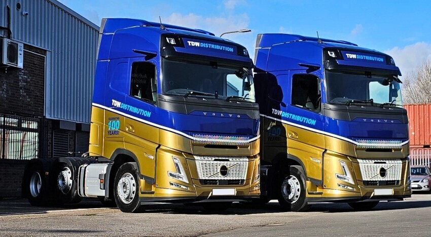 Two Volvo lorry cabs with matching blue and gold vehicle wraps.