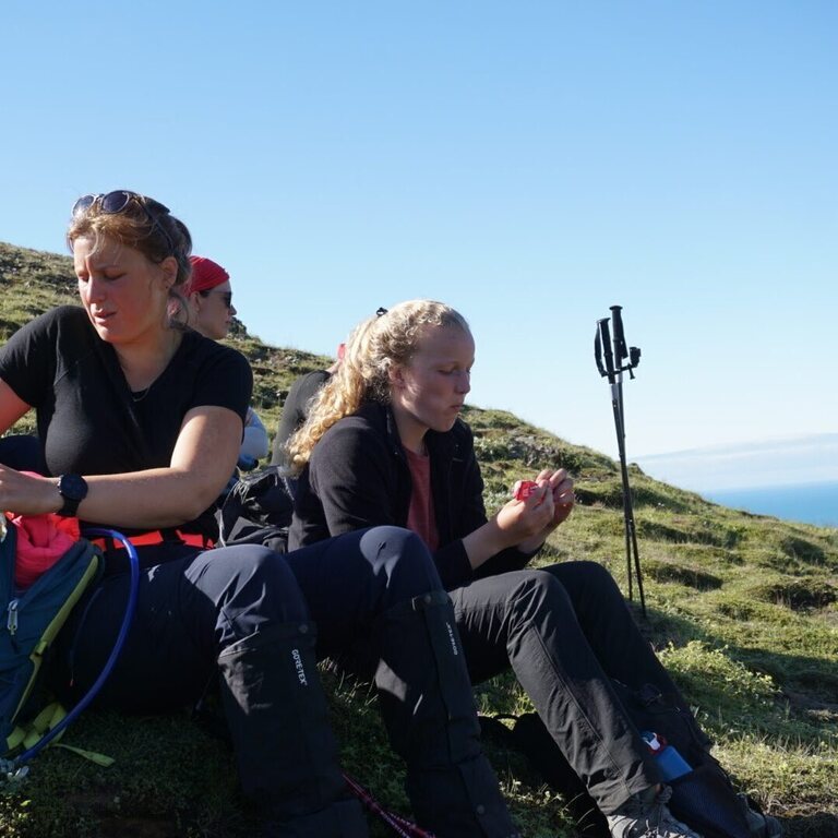 Group of trekkers resting on mossy rock during a multi-day hike in Hornstrandir Nature Reserve, Iceland