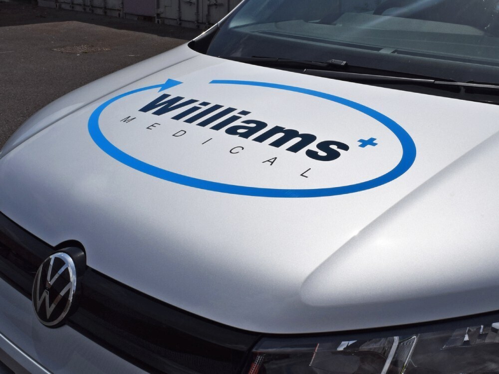 Company branded vinyl graphics logo on front bonnet of silver Volkswagen Caddy.