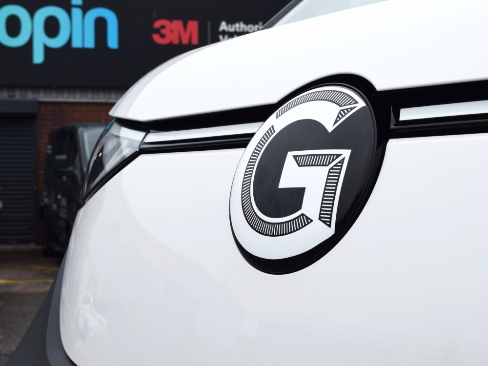 Close up of detailed branded vinyl graphics on front of white Volkswagen ID Buzz electric company vehicle.