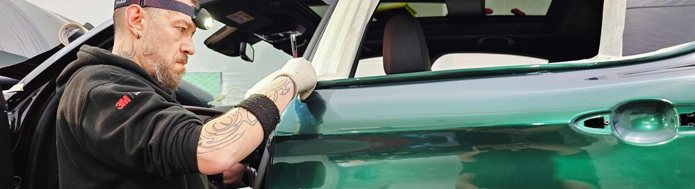 Vehicle wrap technician professionally installing premium vinyl film on a car.