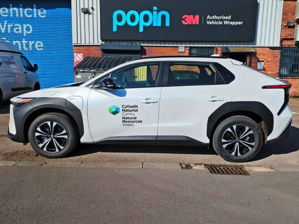 White Toyota BZ4X company car with branded vinyl graphics outside Popin in Cardiff.