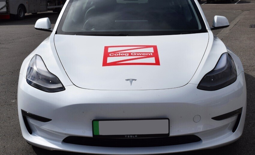 Red branded vinyl graphic on the bonnet of a white leased Tesla car.