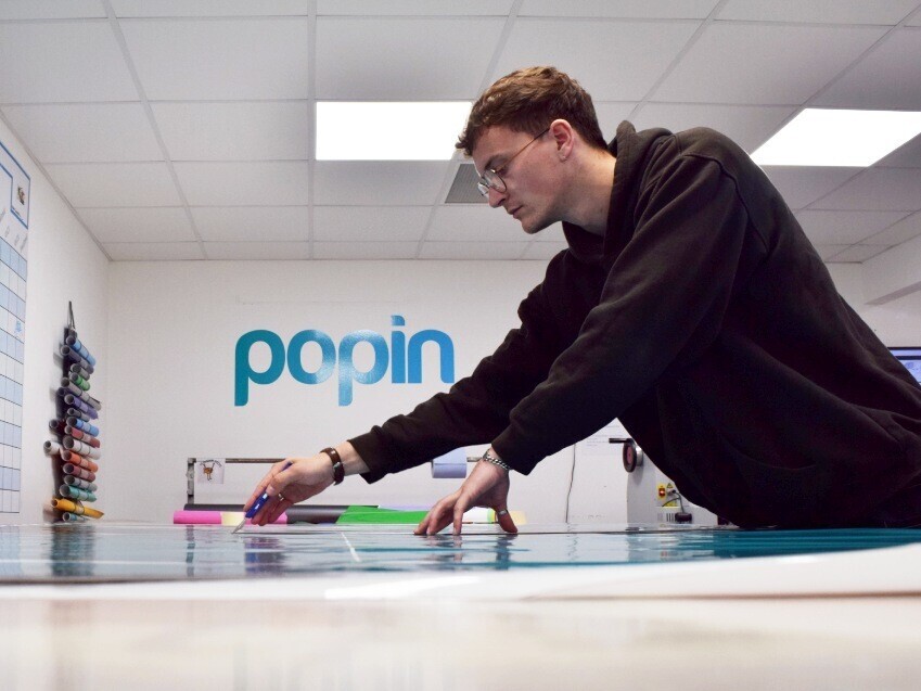 Popin technician cutting vehicle graphics ready for installation on a fleet of company cars.