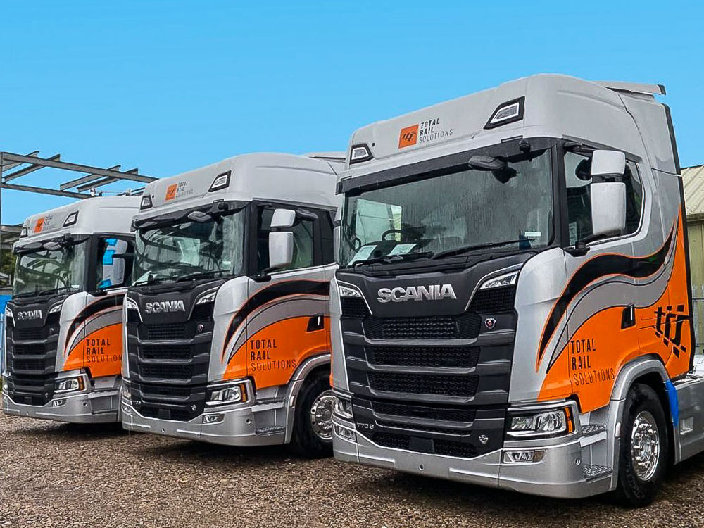 Fleet of Scania S650 trucks with matching orange and silver vehicle wraps and graphics for Total Rail Solutions.