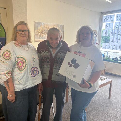 Two activity coordinators stood at Your Care's Dementia Day Club in Bristol, with an elderly gent who donated a bingo set to the day club.