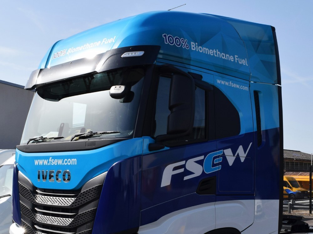 Branded vehicle livery and graphics on a blue Iveco lorry.
