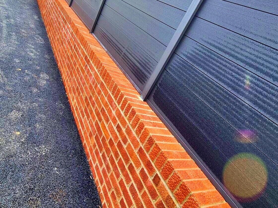 Modern boundary wall design combining a sturdy red brick base with sleek black composite panel fencing. This stylish and durable construction offers both privacy and a contemporary aesthetic, perfect for complementing a variety of property styles.