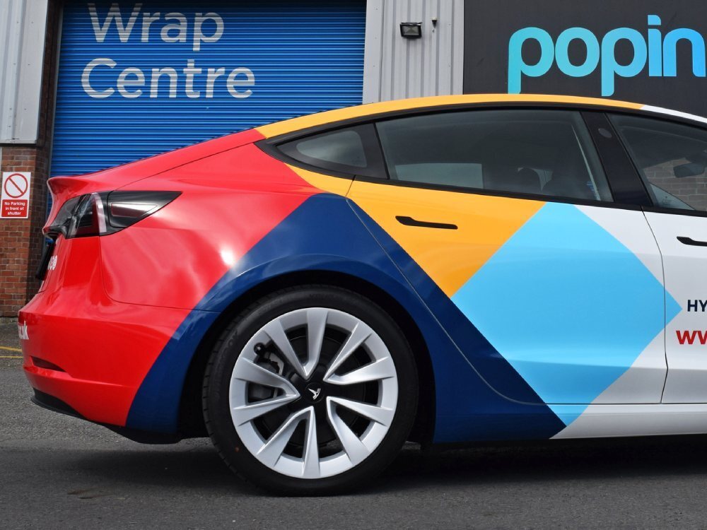 Colourful partial vehicle wrap on rear end of white Tesla Model 3 company car.