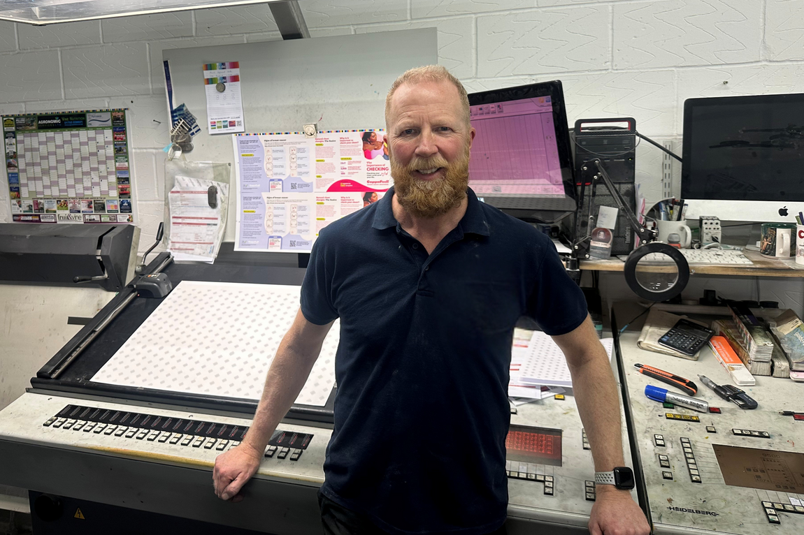 A photo of Spencer standing in front of a printer at Grease Lightning