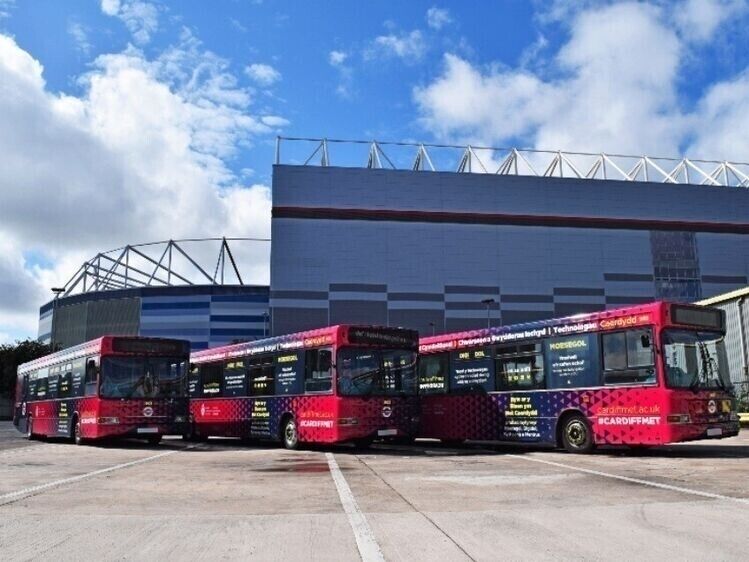 Local Cardiff bus fleet with new vehicle vinyl wraps outside football stadium.